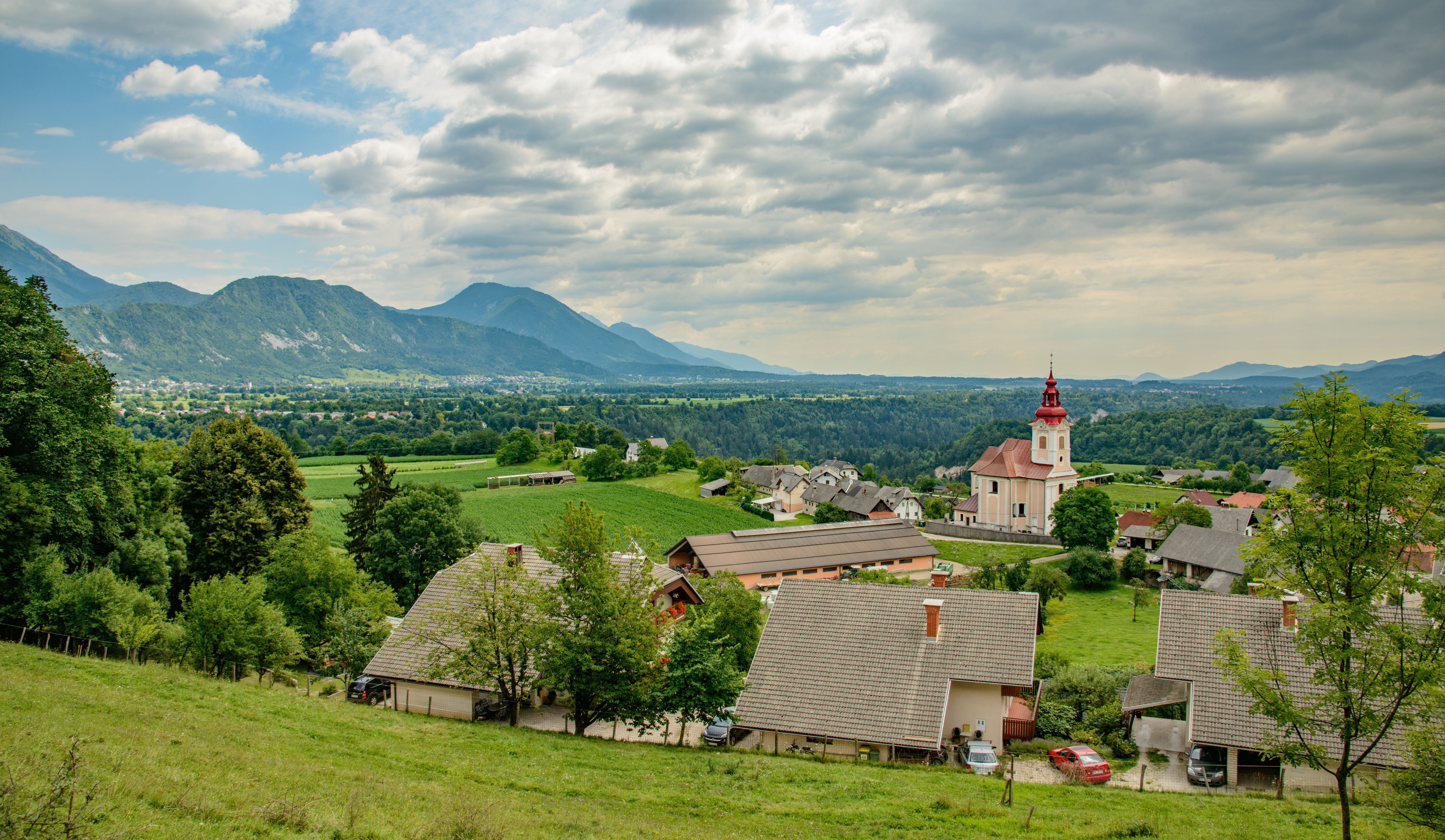 Picturesque village with a church nestled in a lush alpine valley under cloudy skies.