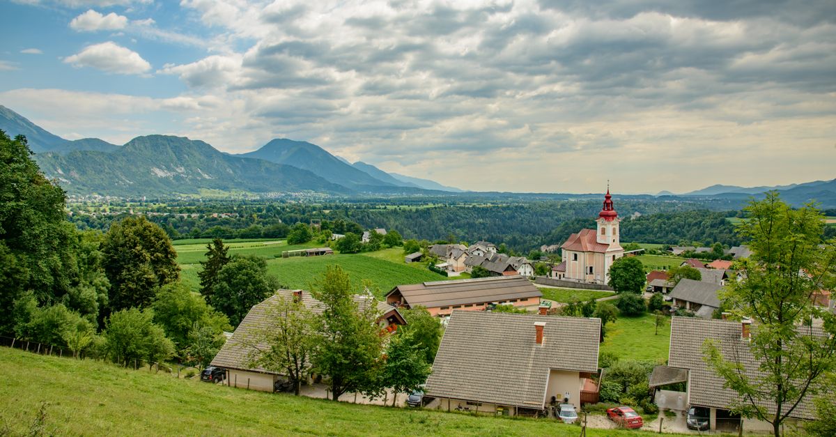Picturesque village with a church nestled in a lush alpine valley under cloudy skies.