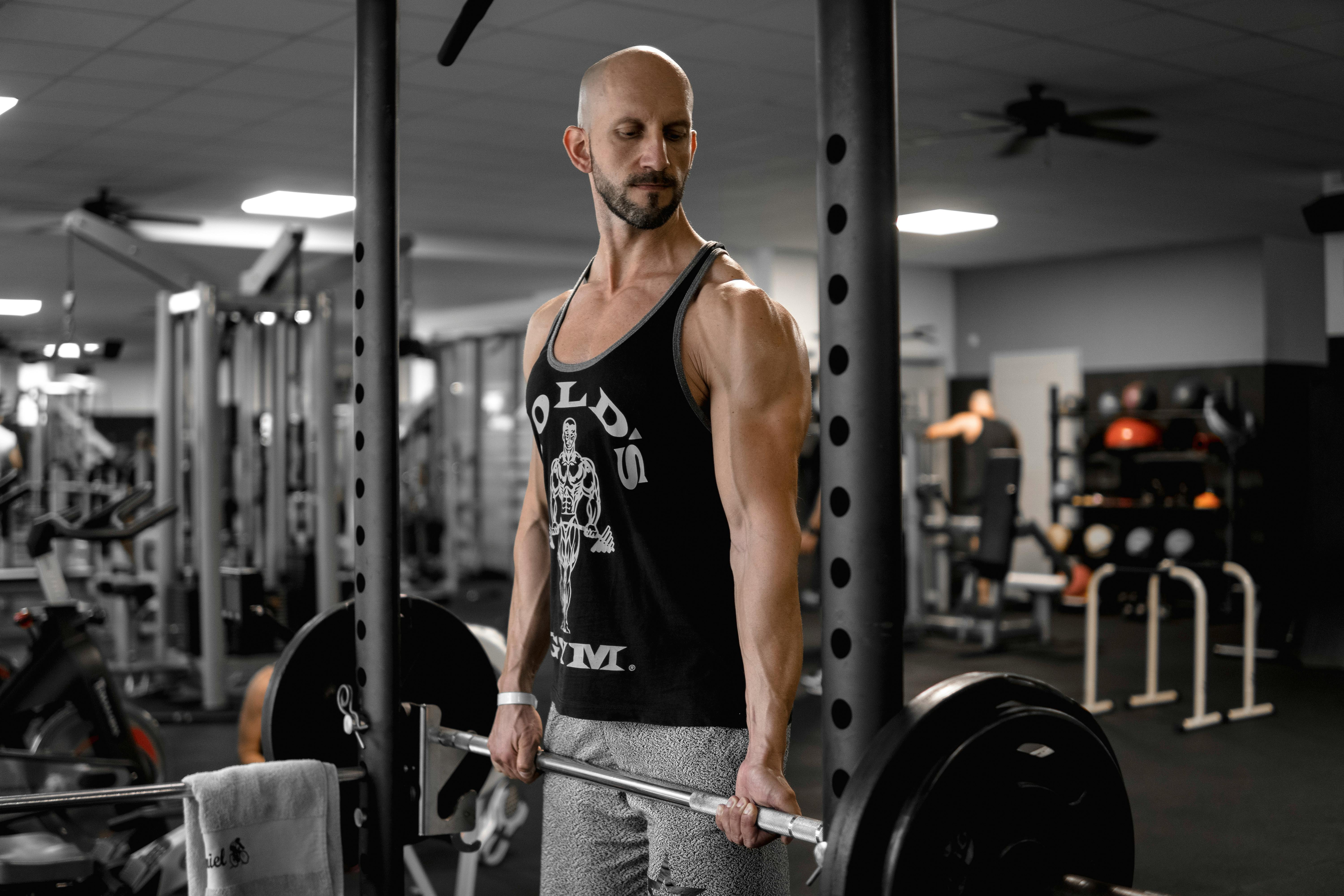 A muscular adult man lifts a barbell at the gym, demonstrating strength and focus.