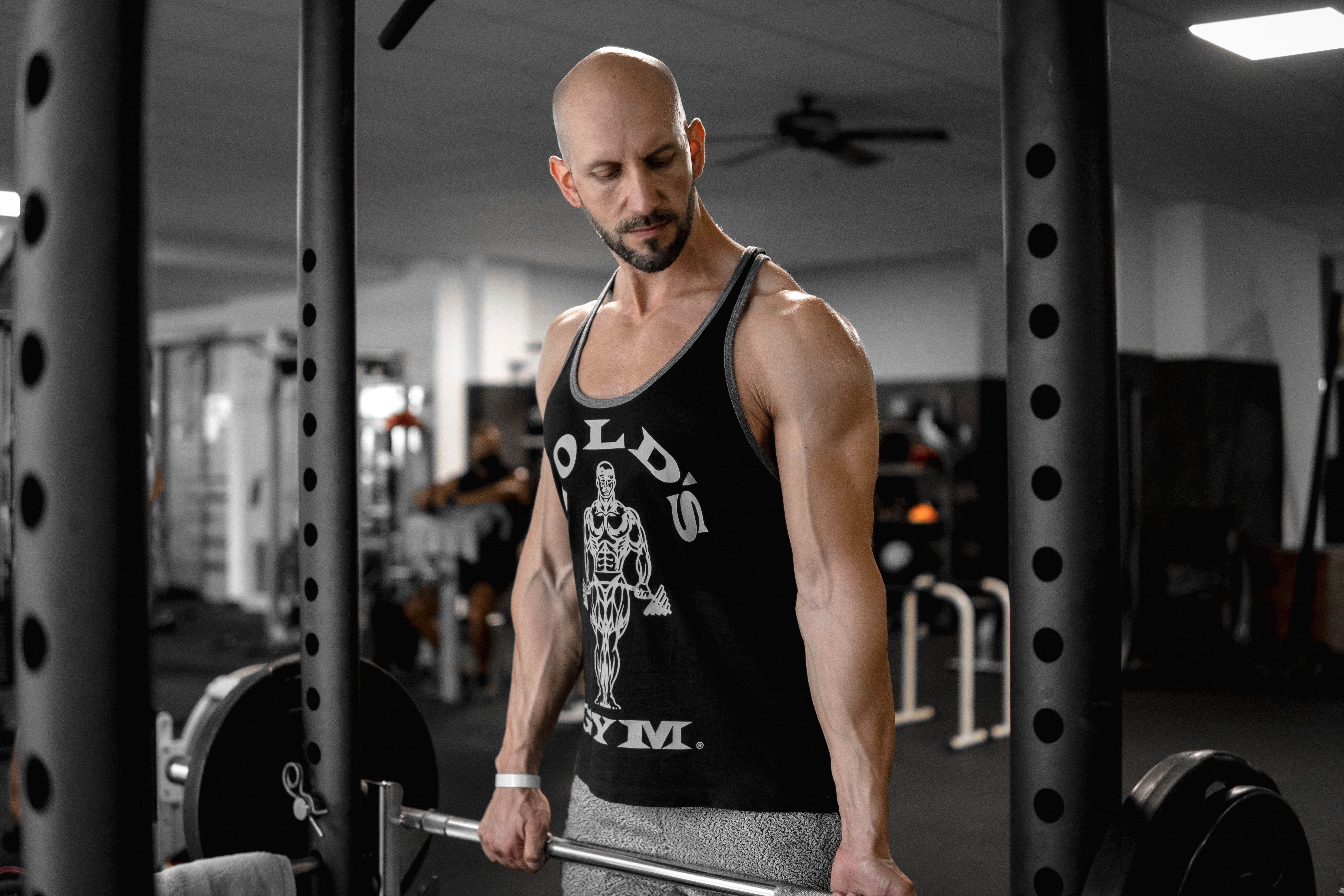Muscular bald man lifting a barbell in a modern gym setting, showcasing strength training.