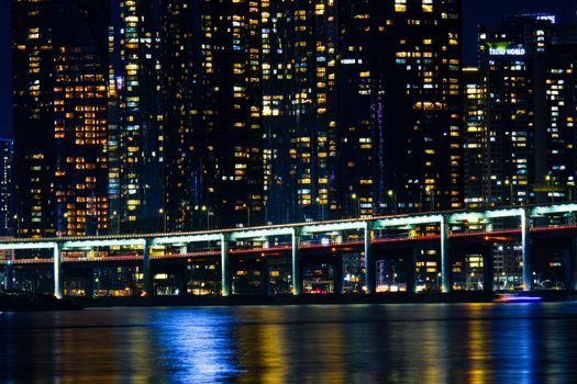 A glowing city skyline with a bridge reflected in calm waters at night.