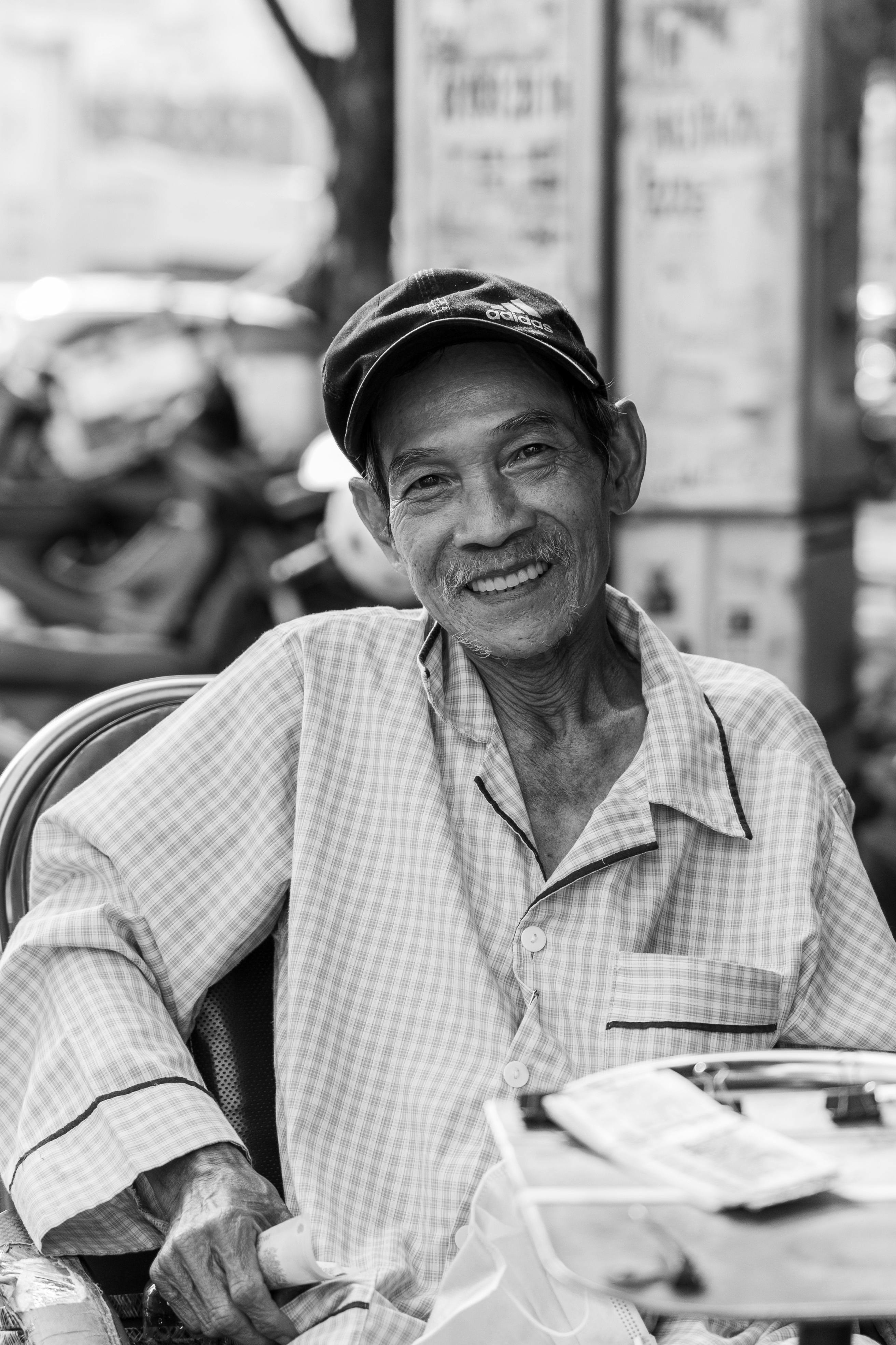 An elderly man smiles while sitting outdoors in Ho Chi Minh City, Vietnam.
