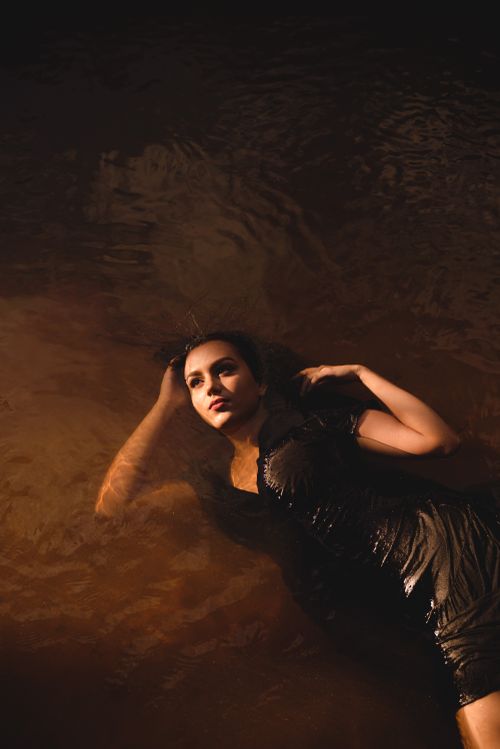 Free A woman in a black dress floats gracefully on a dark water surface, captured from above. Stock Photo