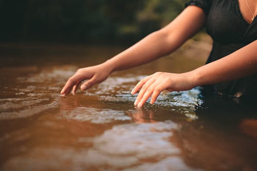 Close-up of Woman Hands Touching Calm Water Surface