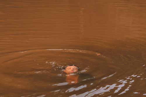 Free A person partially submerged in a warm-toned lake, creating ripples in calm water. Stock Photo