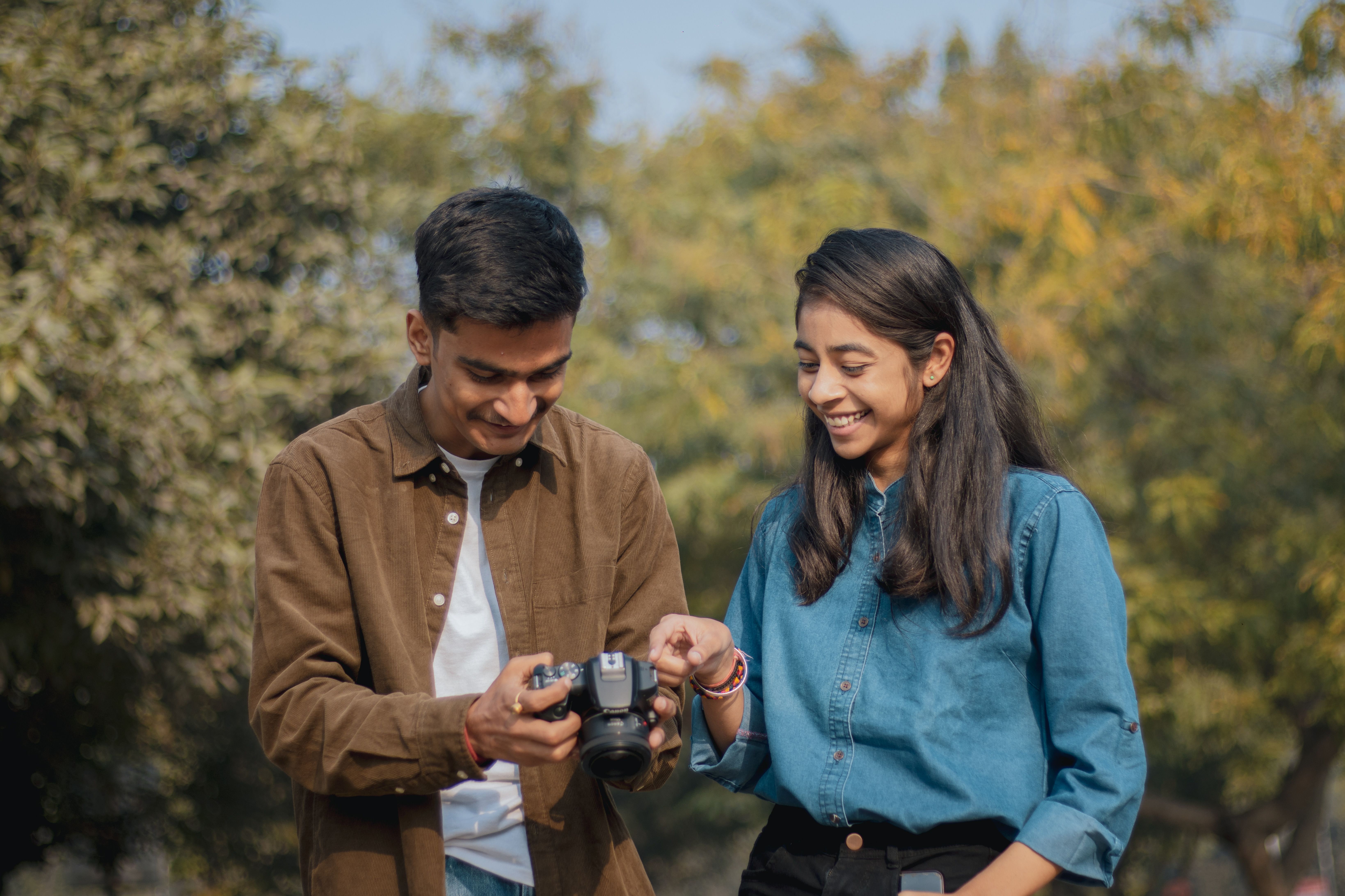 Young man and woman enjoying photography in a park, sharing a DSLR camera experience.