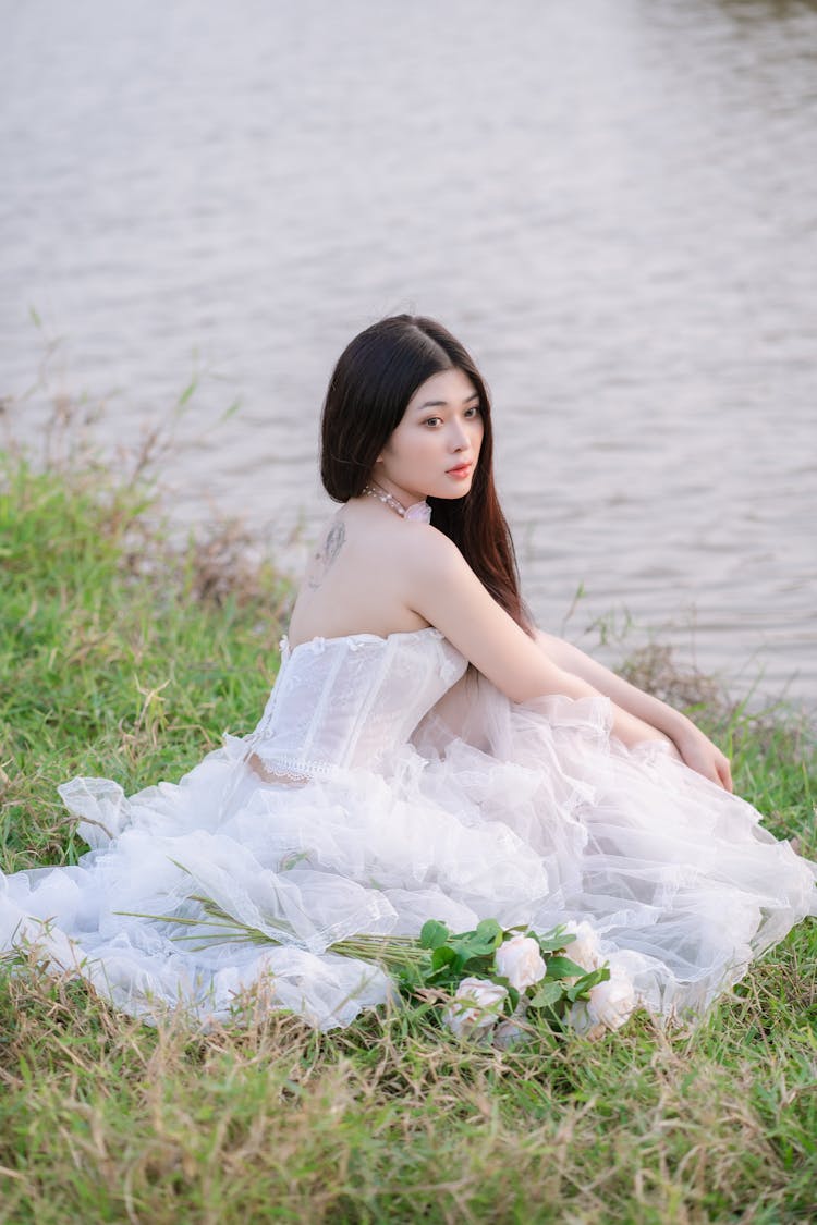 Bride In Dress Sitting On River Bank