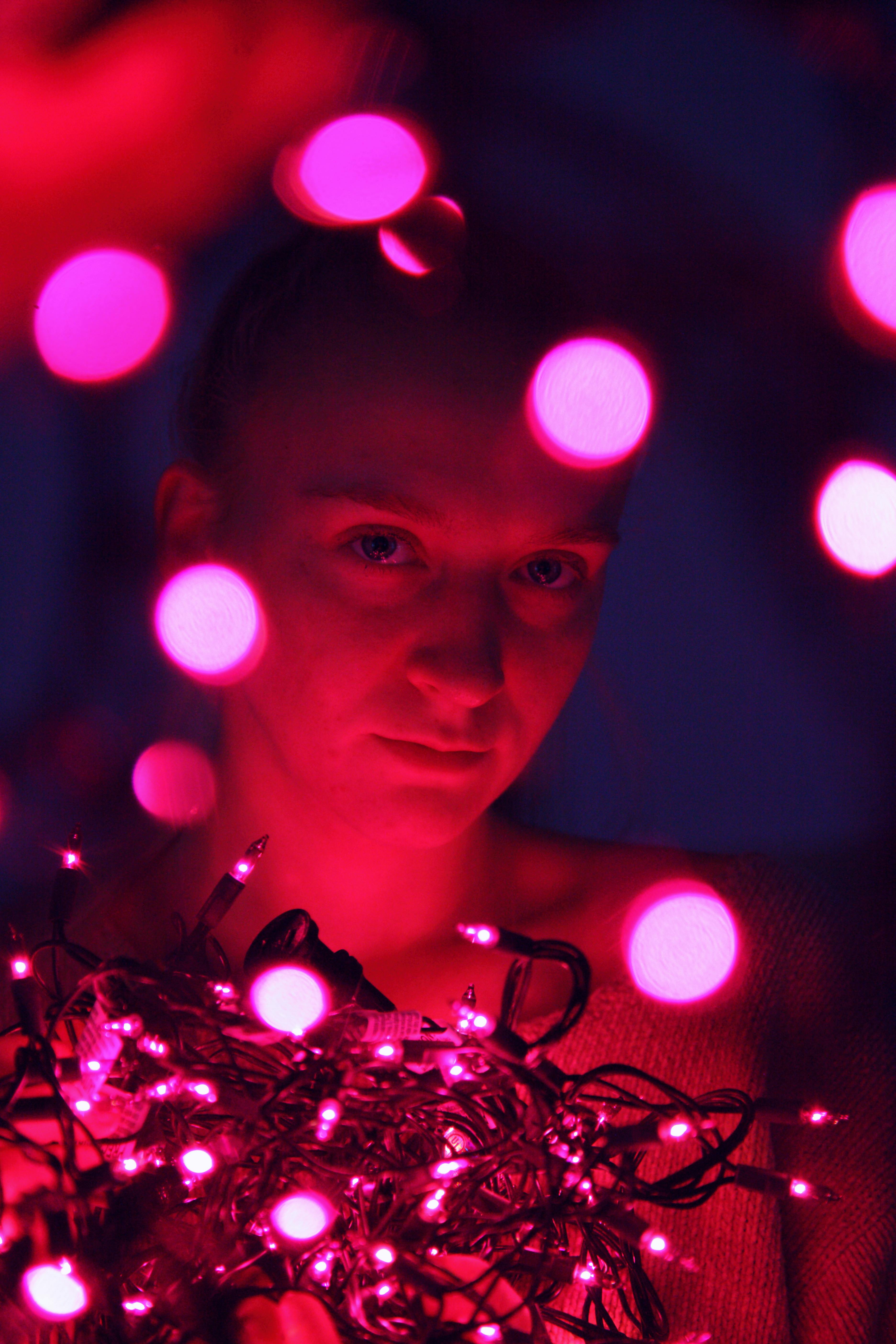 一幅创意肖像描绘了一个被充满活力的粉红色串灯包围的人，并带有散景效果