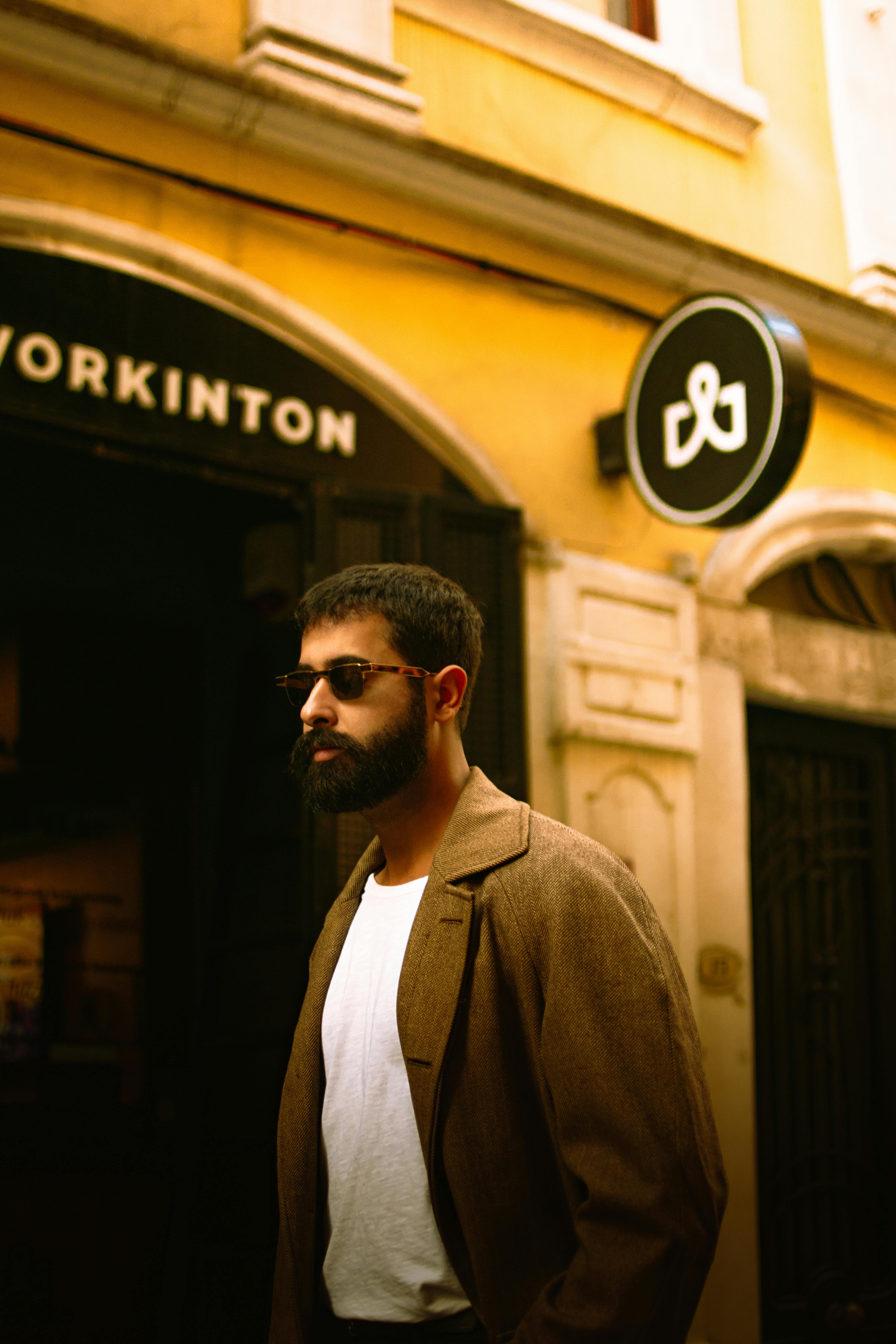 A fashionable man with a beard and sunglasses walks past elegant buildings in İstanbul.