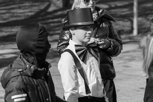 A young performer dressed elegantly with a top hat and bow tie interacts with others on the street.