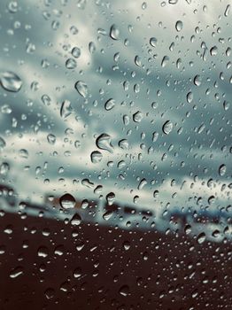 Close-up view of rain droplets on a window with a cloudy sky background, capturing the mood of a rainy day.