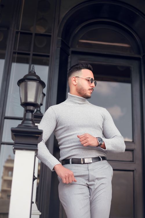 Free Fashionable man in gray attire poses confidently against an urban backdrop. Stock Photo