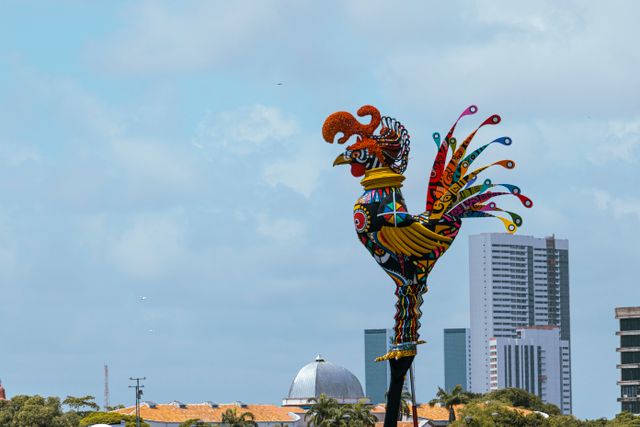 Vibrant rooster sculpture overlooking Recife skyline, capturing Brazilian culture.