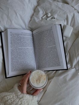 An inviting scene of a book, a cup of coffee, and earbuds on a bed.