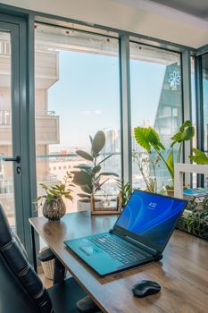 A bright modern office setup with a laptop and cityscape view through large windows.