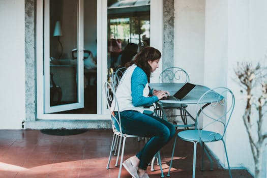 Young woman working on laptop at a stylish patio table outside a home setting.