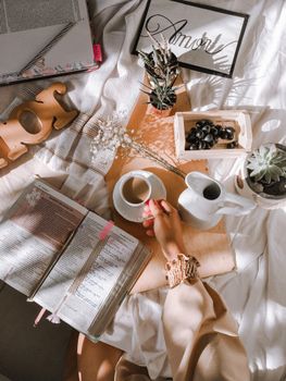 A serene flat lay showing a hand with coffee, books, and decor on a textured surface.