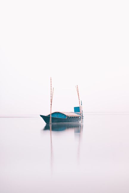 A serene scene of a lone boat floating on foggy waters in Chilmari, Bangladesh.