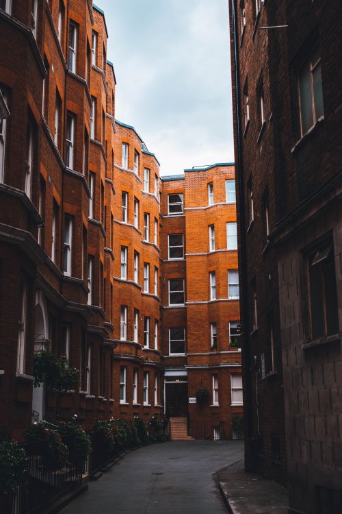 Free Charming narrow alleyway in Greater London flanked by historic brick apartments under cloudy skies. Stock Photo