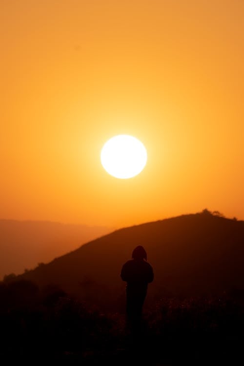 A silhouette of a person standing on a hill with the sun setting behind them