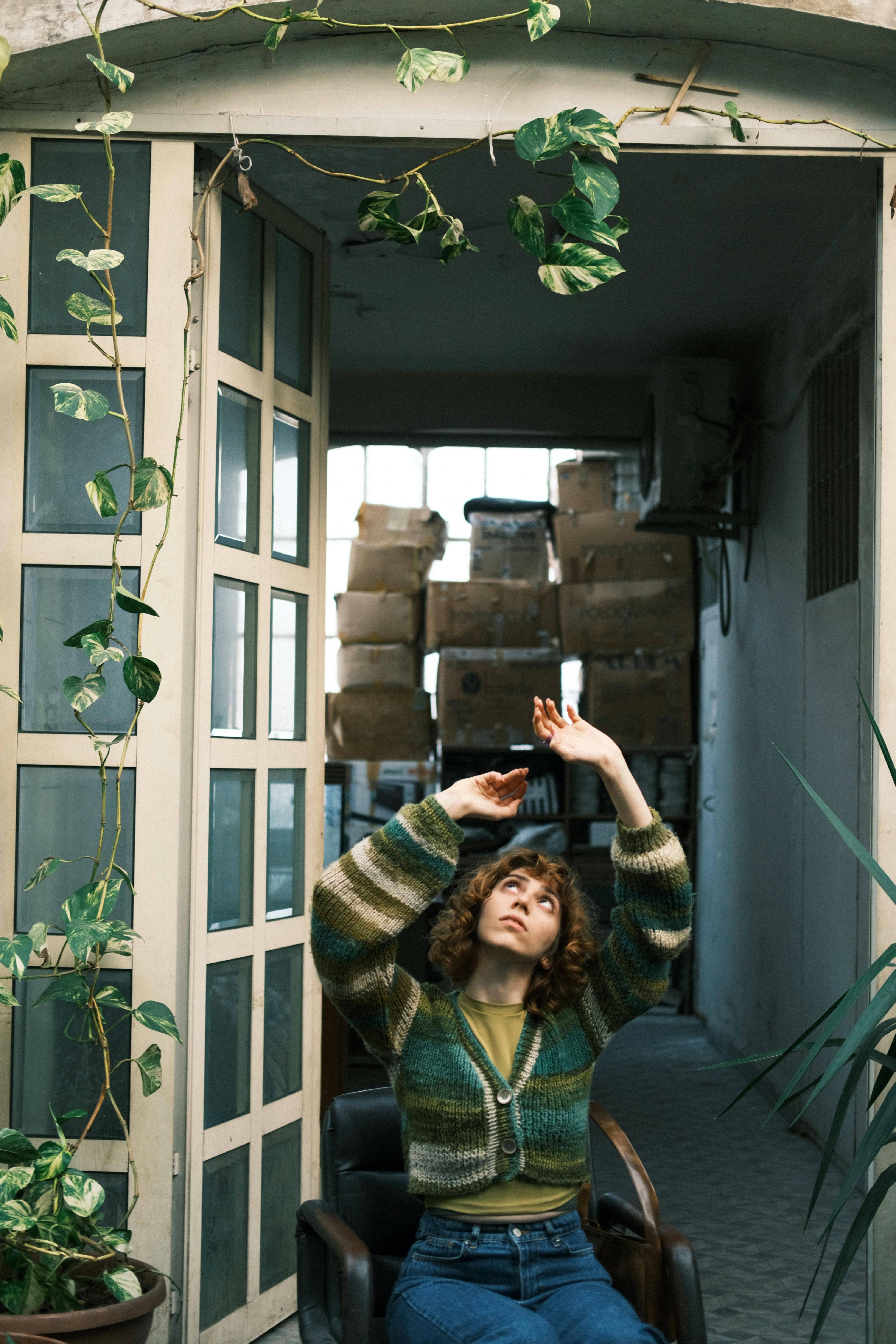 Woman sitting on a chair in a plant-filled indoor space, creating a serene atmosphere.