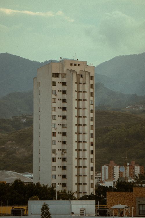 Free Tall residential building surrounded by mountains under a cloudy sky. Stock Photo