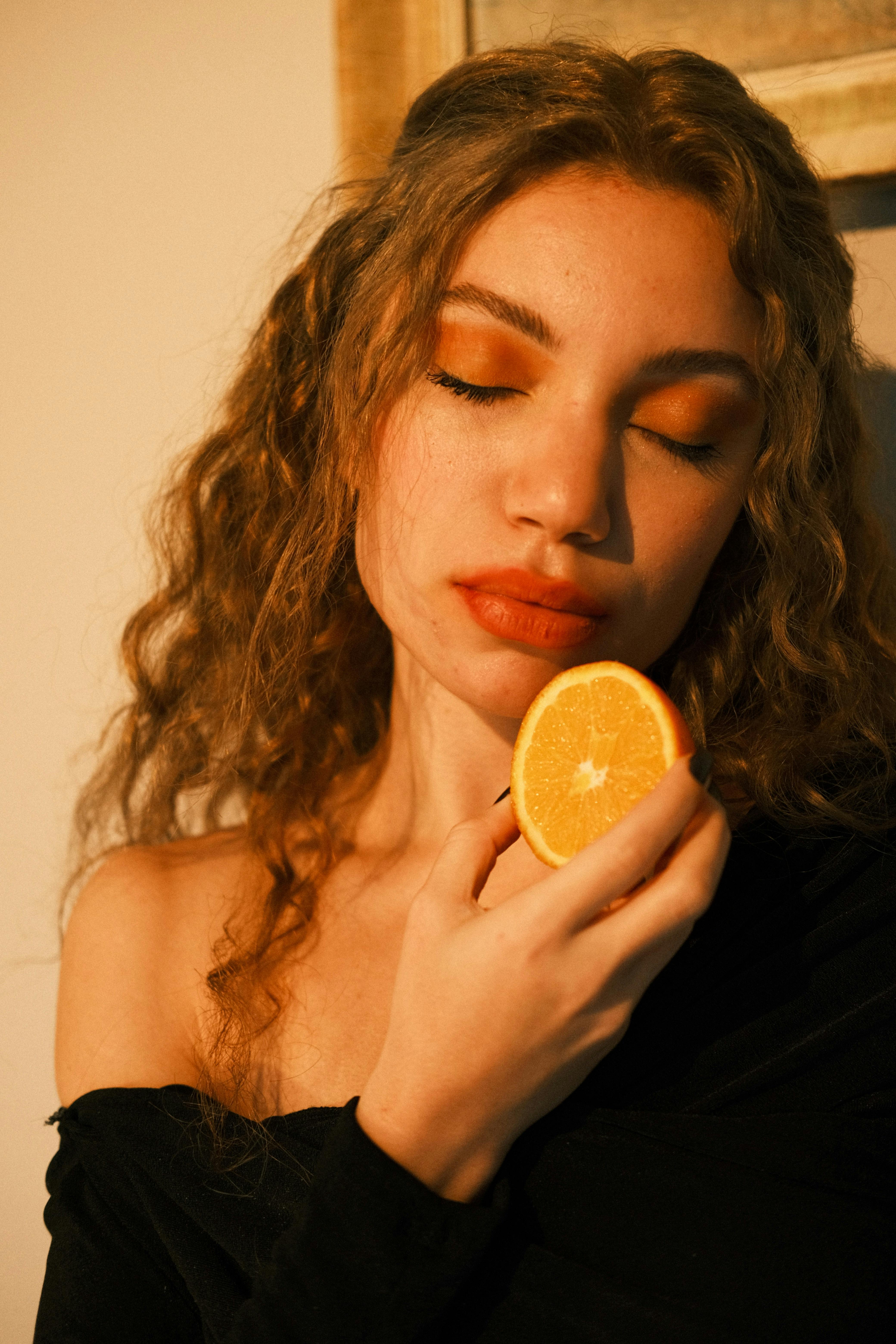 Artistic portrait of a young woman holding a fresh orange slice with warm, natural lighting.