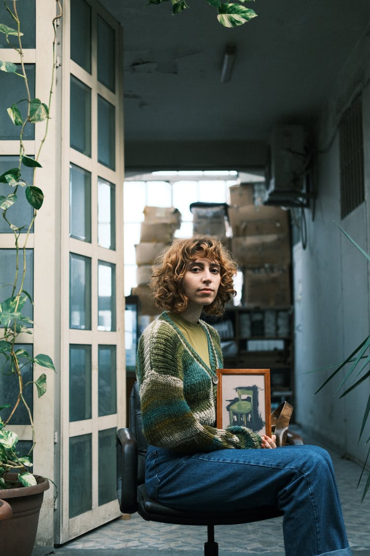 Young Woman Holding A Framed Picture Sitting On A Chair On A Pavement 