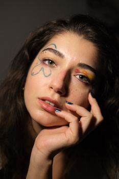 Artistic portrait of a young woman with creative colorful makeup in studio lighting.