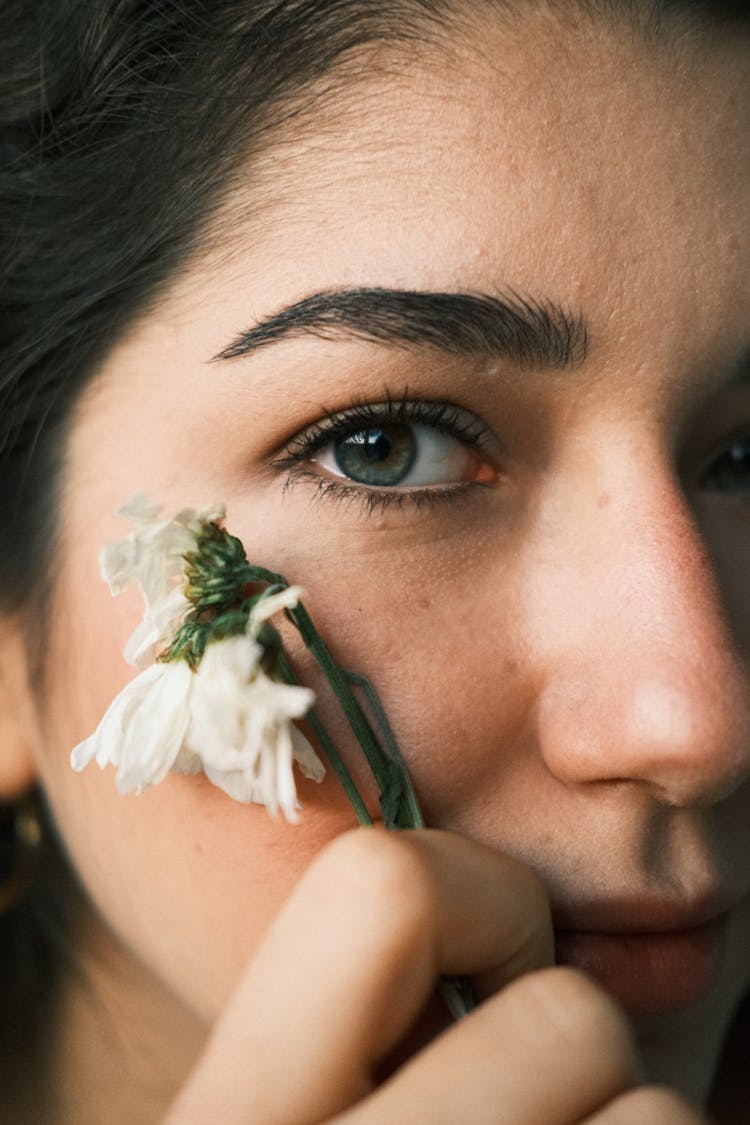 Closeup Of A Young Brunette Holding A Flower Next To Her Cheek