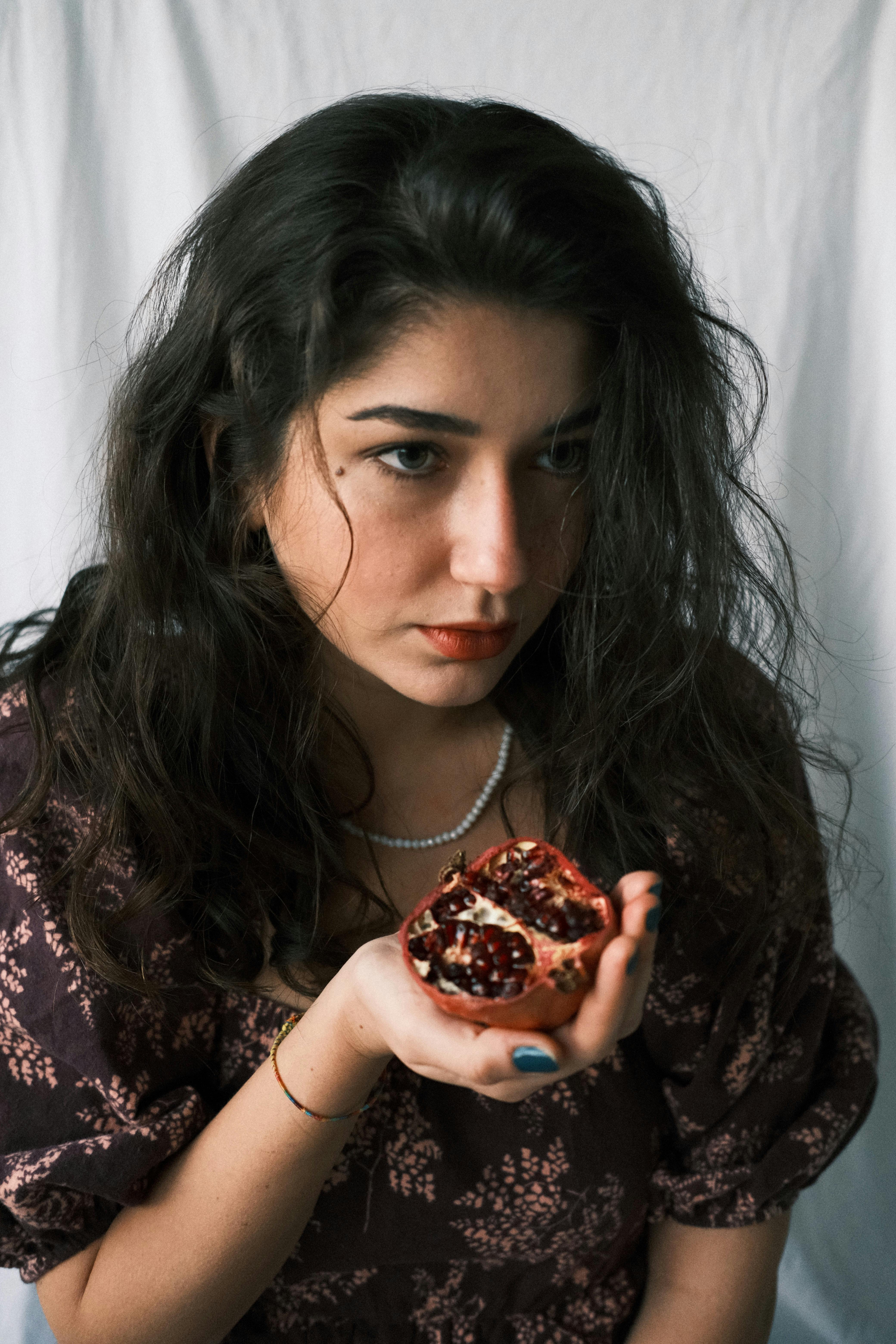 Close-up portrait of a young woman holding a pomegranate, indoors setting.