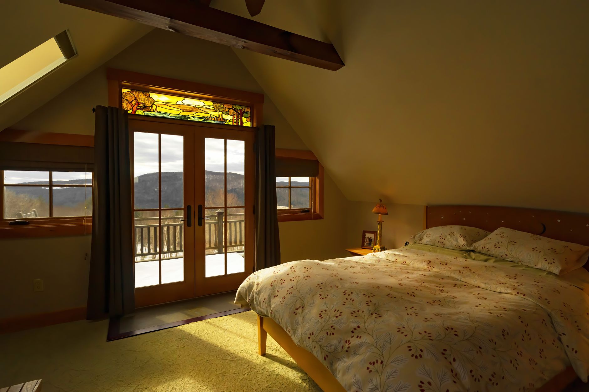 A warm and inviting bedroom with a balcony overlooking nature, bathed in sunlight.
