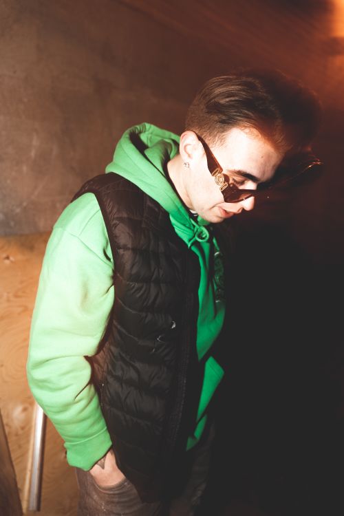Free Stylish young male rapper posing with sunglasses and green hoodie, exuding a cool urban vibe. Stock Photo
