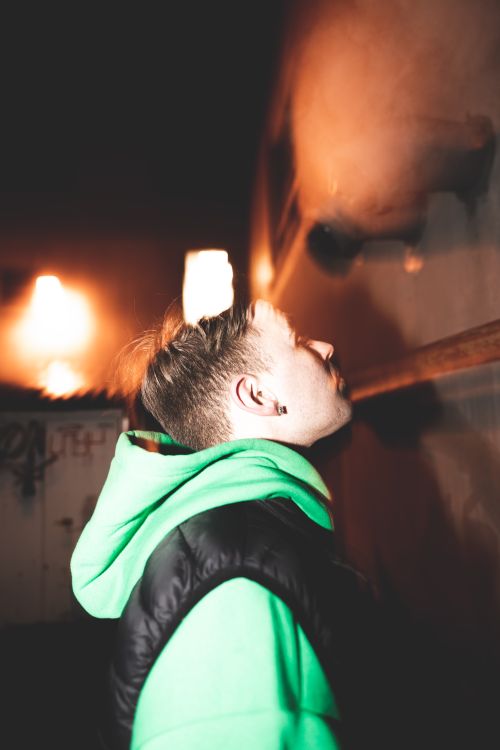 Free A moody portrait of a man in a green hoodie indoors, captured under dim lighting. Stock Photo