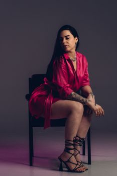 A fashionable woman in a pink dress poses on a chair in a studio. Stylish and modern look in vertical composition.
