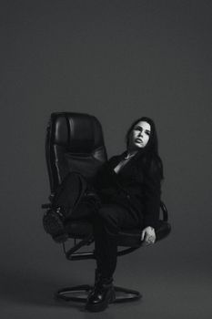 Black and white portrait of a woman posing in a revolving chair in a studio.