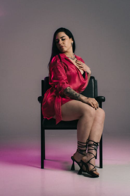 Studio Shot of a Woman in a Dress and Heels Sitting on a Chair 