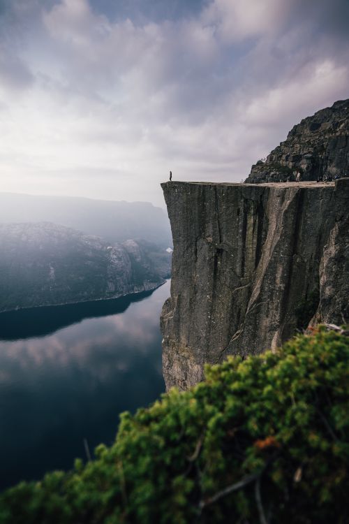 Free A lone adventurer stands on the edge of Preikestolen cliff, overlooking the stunning fjord below in Norway. Stock Photo