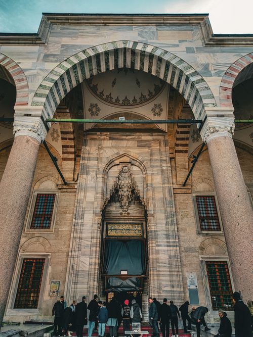 Free Low angle shot of a historic mosque entrance showing ornate arches and gathered people. Stock Photo
