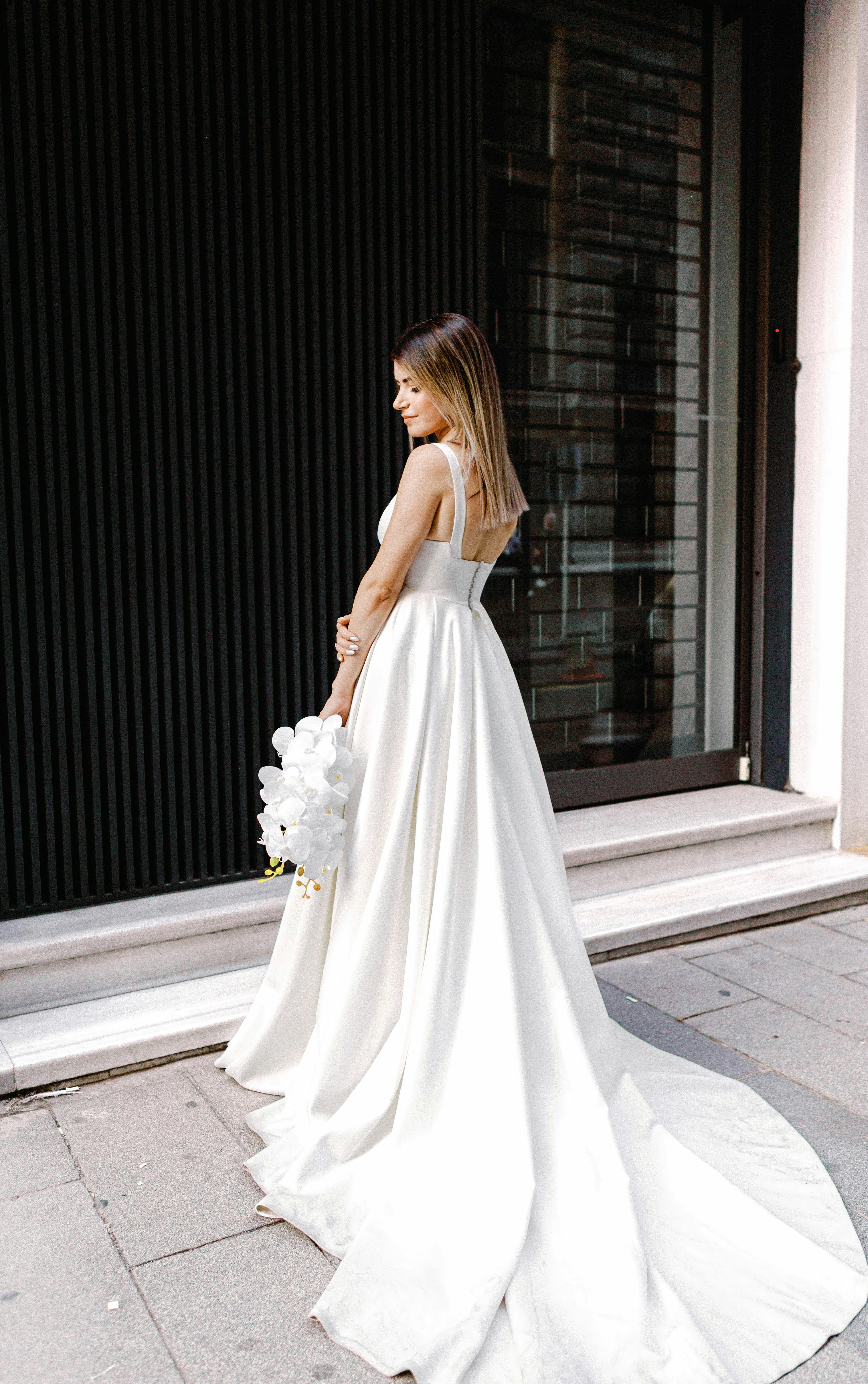 Bride in a beautiful white dress holding bouquet outside stylish building.