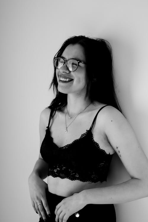 Smiling Woman in Lingerie and Glasses Posing near Wall