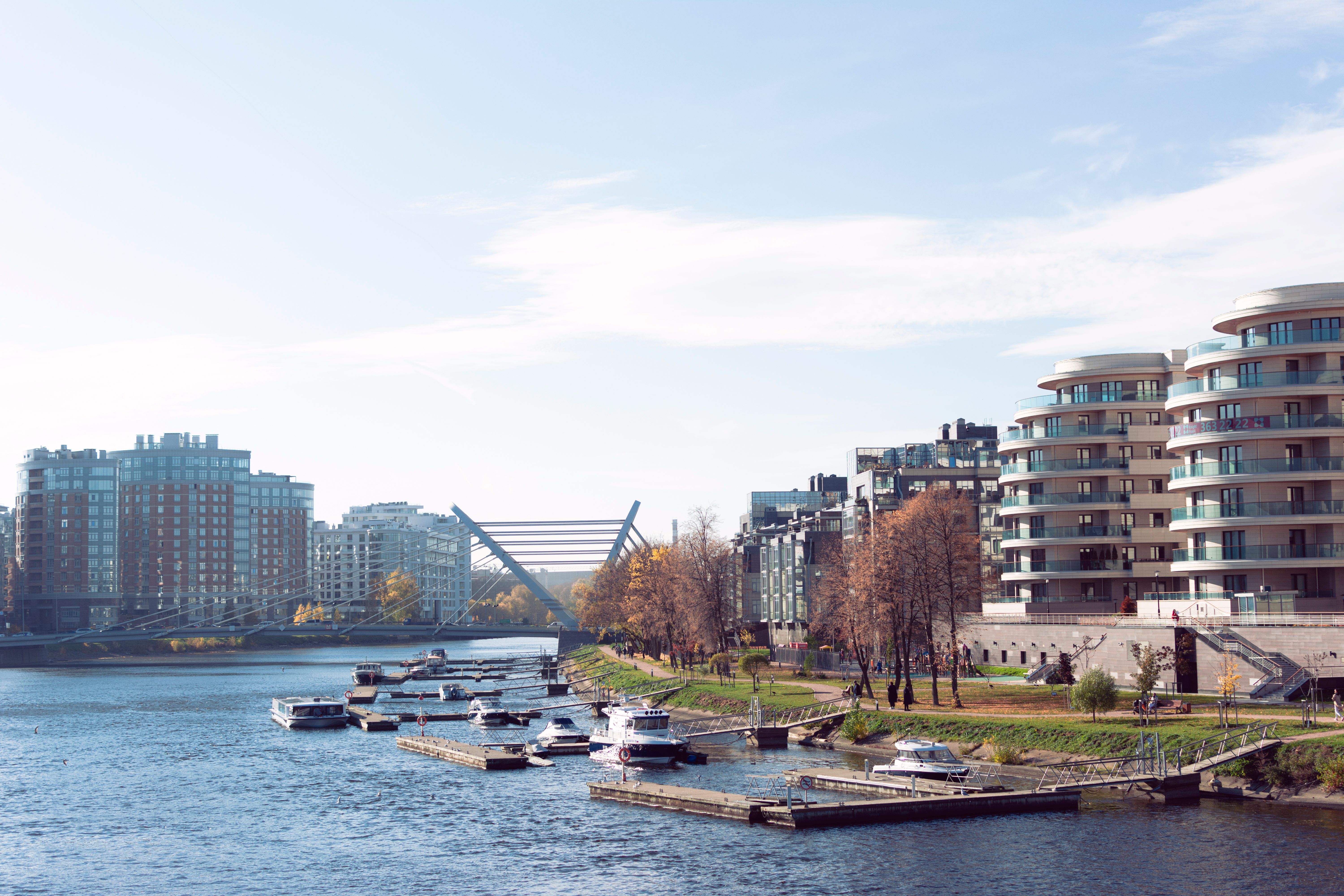Scenic view of urban riverfront with moored boats, modern apartments, and a distinctive bridge.