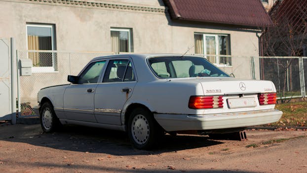 Classic white Mercedes-Benz sedan parked near a suburban house on a sunny day.