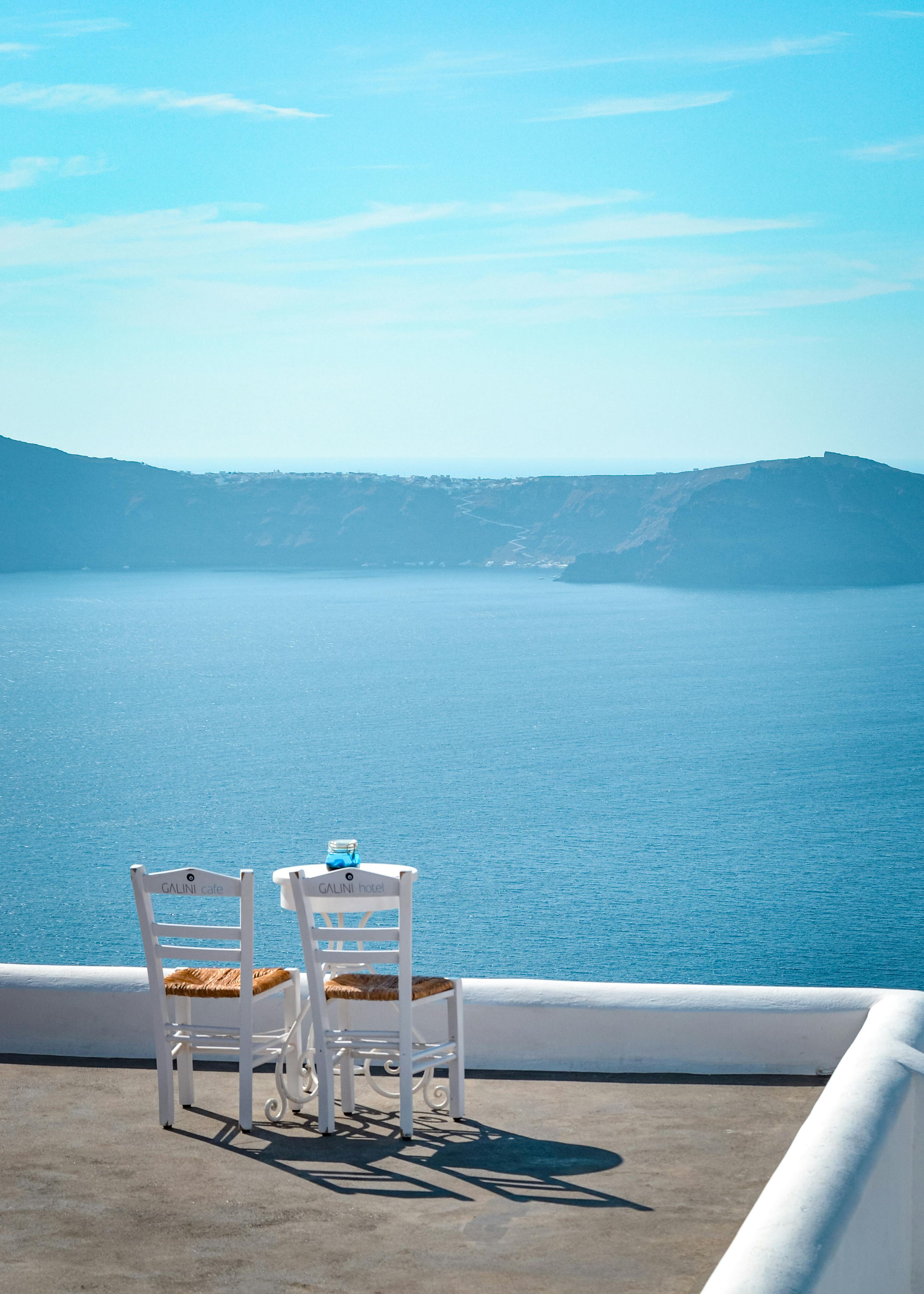 Idyllic view of Aegean Sea from terrace in Thera, Greece with empty chairs and table.