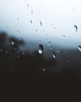 Close-up of raindrops on glass with blurred outdoor view, creating a moody atmosphere.