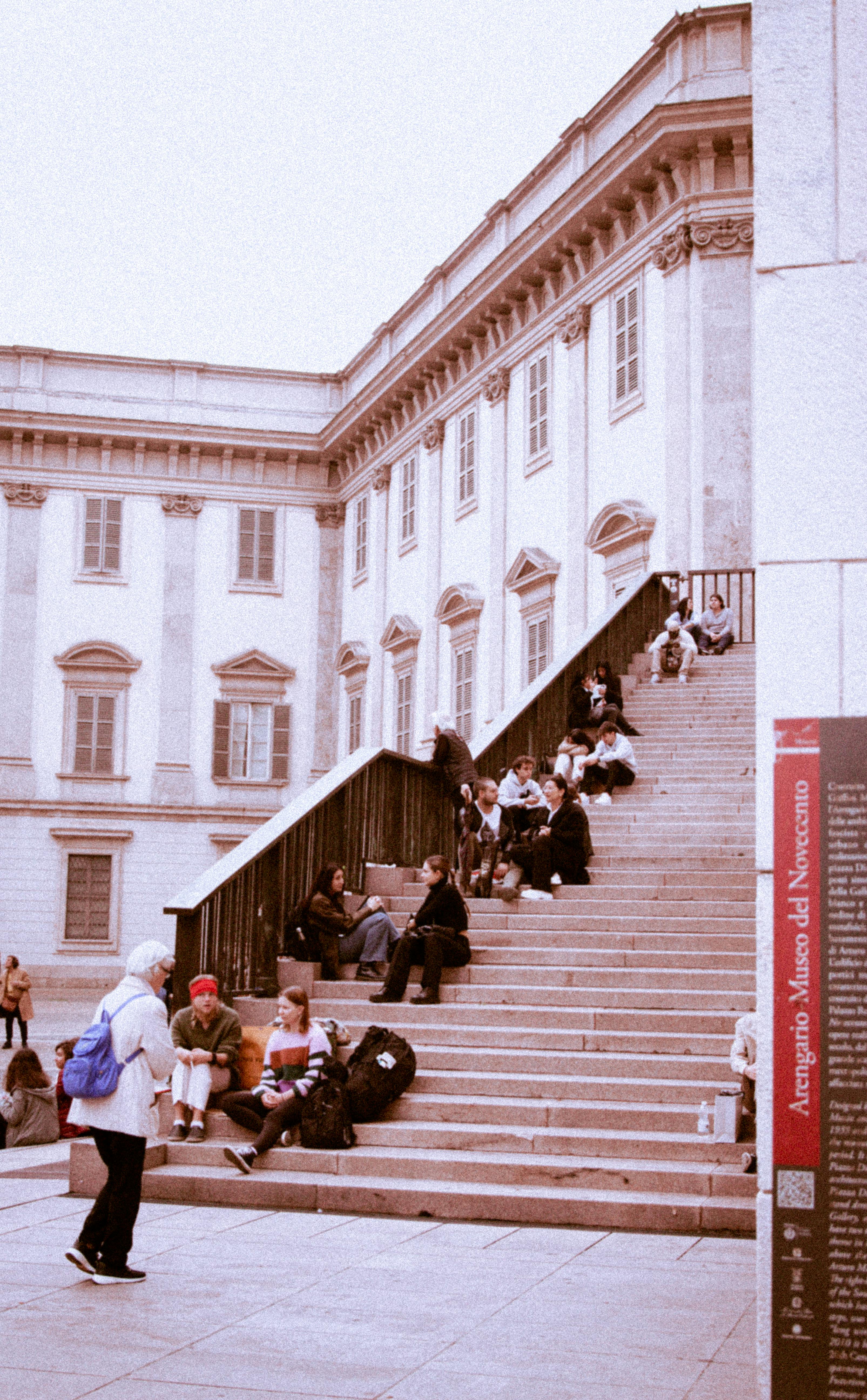 Tourists gather on the steps of Milan's Royal Palace, capturing its neoclassical architecture.