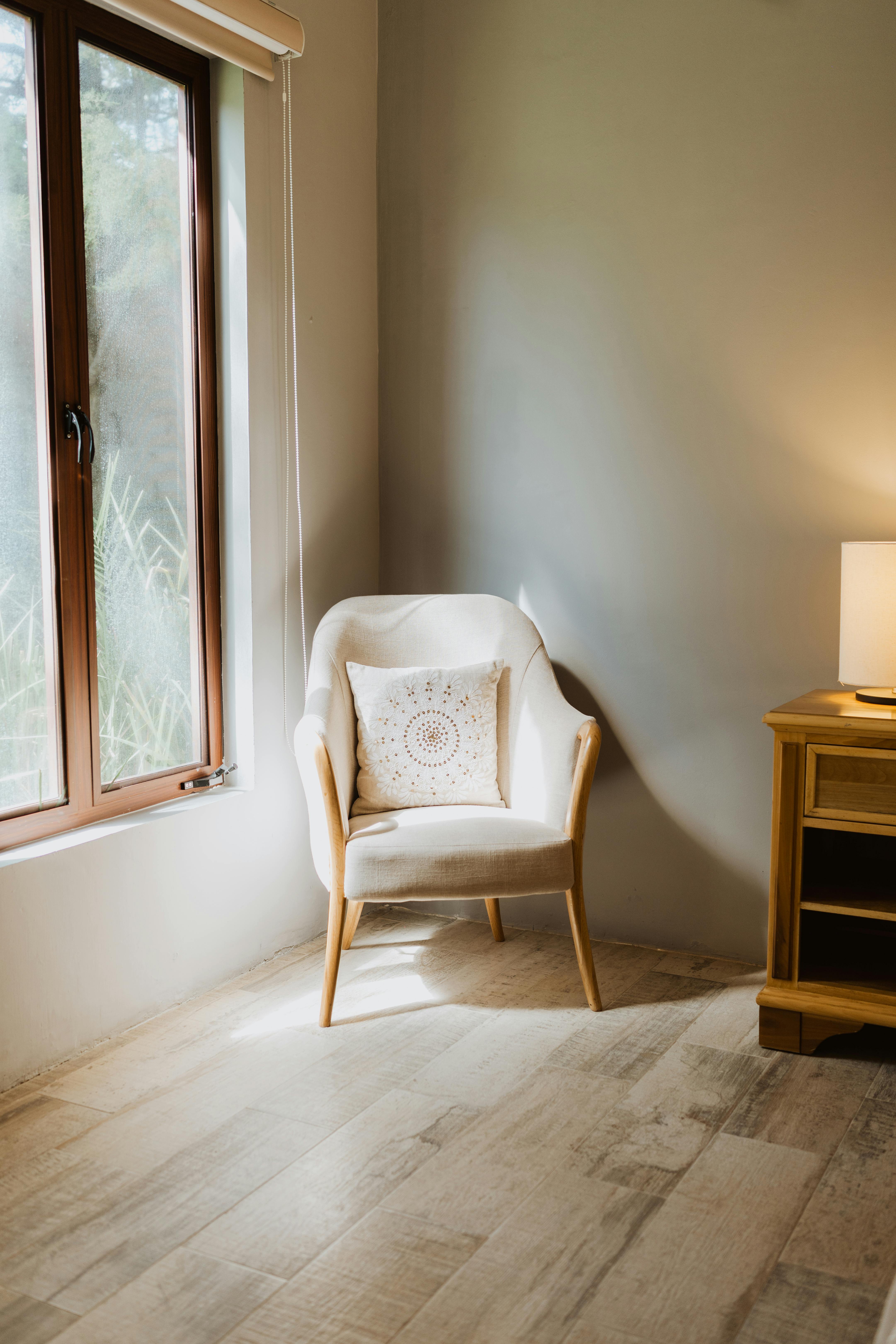 Cozy white armchair by window in a minimalist, sunlit interior with wooden flooring.