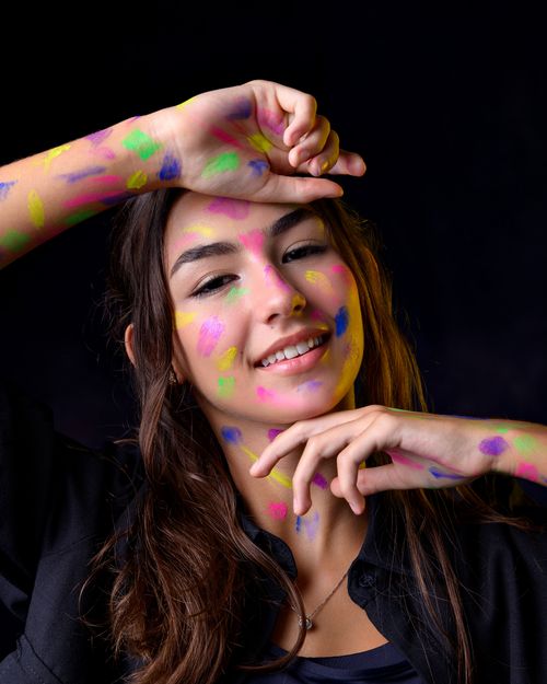 Free A joyful portrait of a young woman with colorful face paint on a dark background. Stock Photo