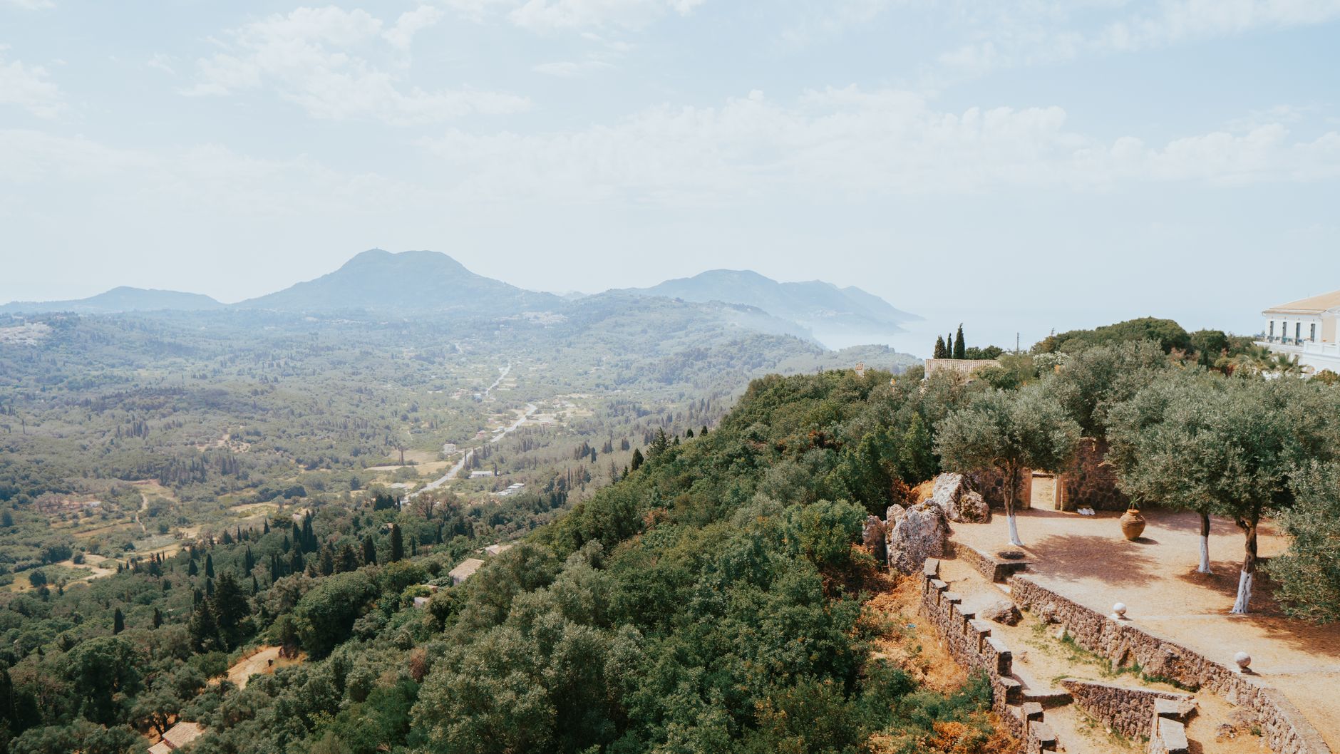 Breathtaking aerial view of Kerkyra's lush landscape with hills, valleys, and ancient structures under a clear sky.