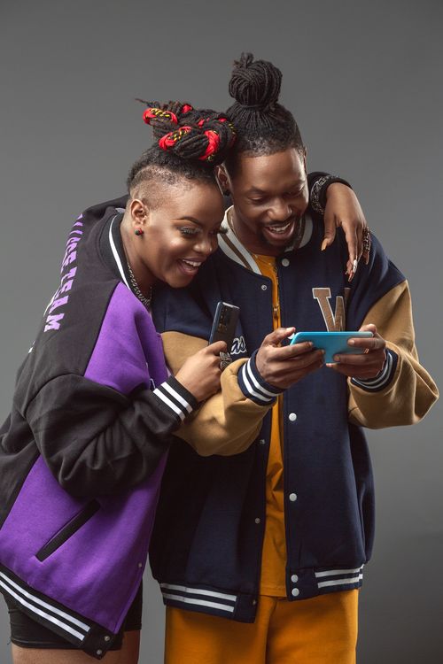 Free A joyful young couple using smartphones together, showcasing modern fashion and connectivity. Stock Photo
